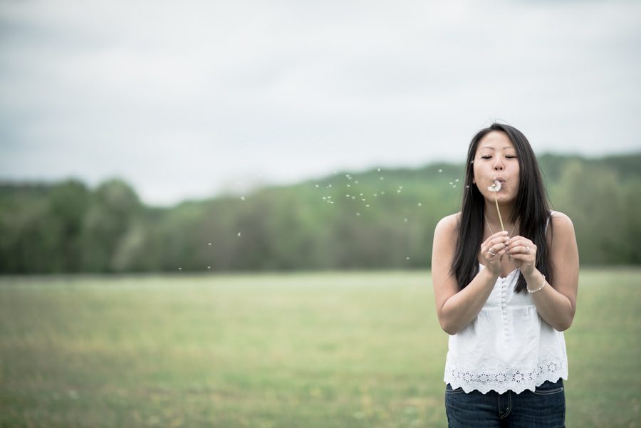 Kelly blows on dandelions during her engagement session in Hunterdon, NJ. Captured by awesome NJ wedding photographer Ben Lau.