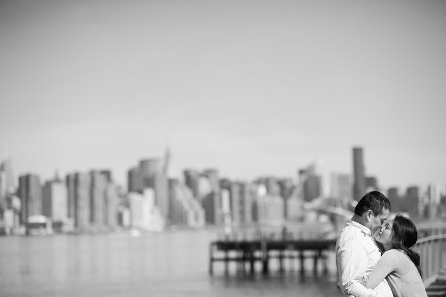 Lisa and Kai embrace on a pier with the NYC skyline in the background during their engagement session in Williamsburg with awesome New York City wedding photographer Ben Lau.