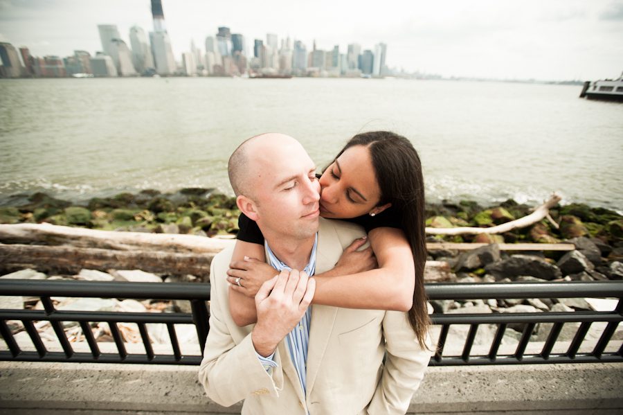 Patrice kisses Josh from behind with NYC in the background during their engagement session in Jersey City, NJ with awesome NJ wedding photographer Ben Lau.