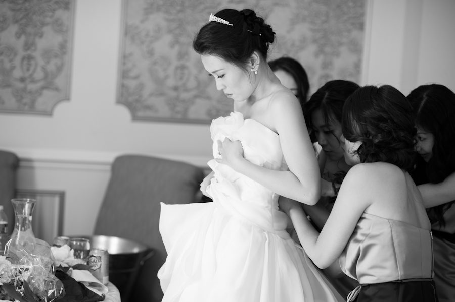 Bridesmaids help bride into dress on her wedding day at Snug Harbor in Staten Island. Captured by awesome New York City wedding photographer Ben Lau.