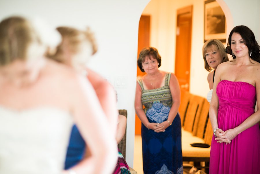 Friends and family of bride look on as she puts on her dress. Captured by Caribbean destination wedding photographer Ben Lau.