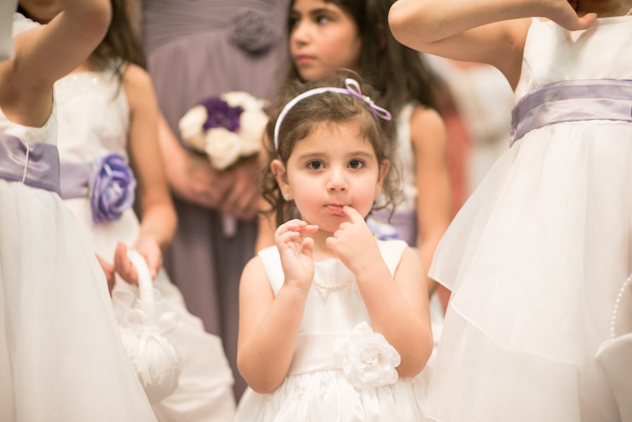 Flower girl looks at the camera during a wedding ceremony in Jersey City, NJ. Captured by awesome NJ wedding photographer Ben Lau.