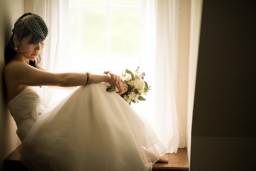 Bride Yulan sits by the window before here wedding ceremony at the Mountain Lakes House in Princeton, NJ. Captured by awesome NJ wedding photographer Ben Lau.