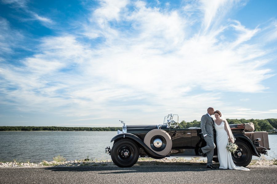 Bride and groom stand by their antique car on the causeway, en route to their wedding reception at the Rams Head Inn on Shelter Island, NY.