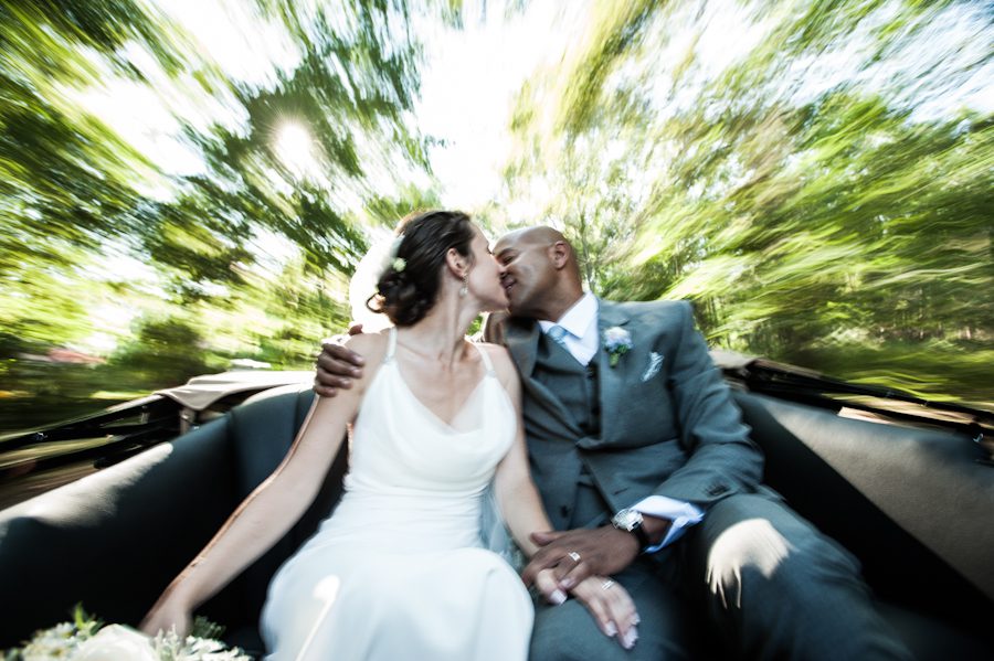 Bride and groom kiss under the trees on the back of their convertible antique car, en route to their wedding reception at the Rams Head Inn on Shelter Island, NY.