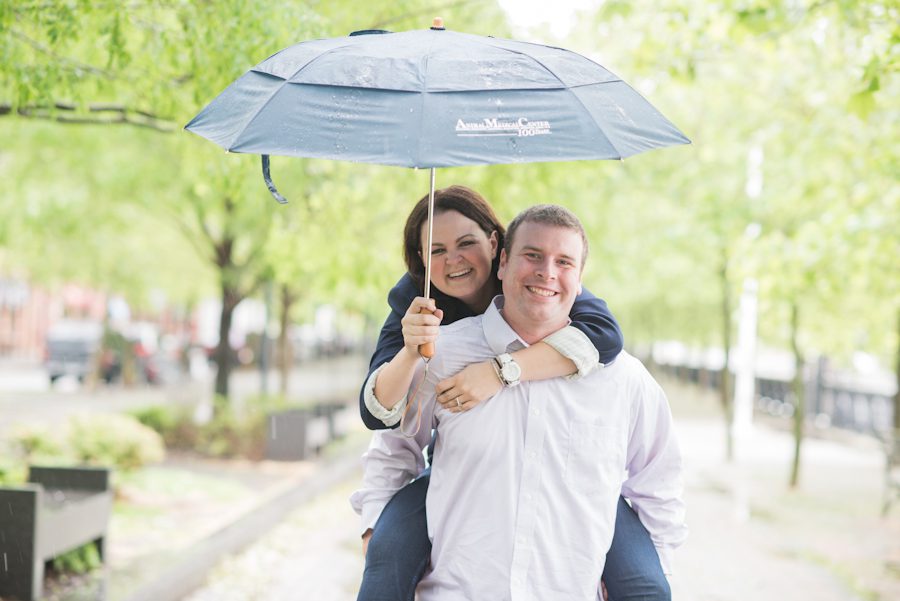 Piggy back ride under an umbrella during a rainy engagement session in Hoboken, NJ. Captured by awesome NJ wedding photographer Ben Lau.