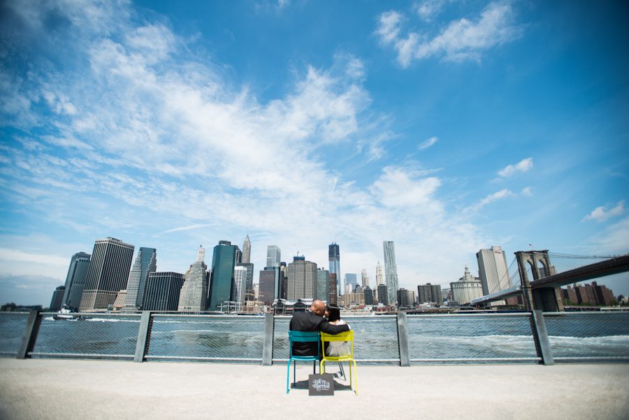 Couples sit on chairs during their faux engagement session at Brooklyn Bridge Park.. Captured by awesome NJ wedding photographer Ben Lau.