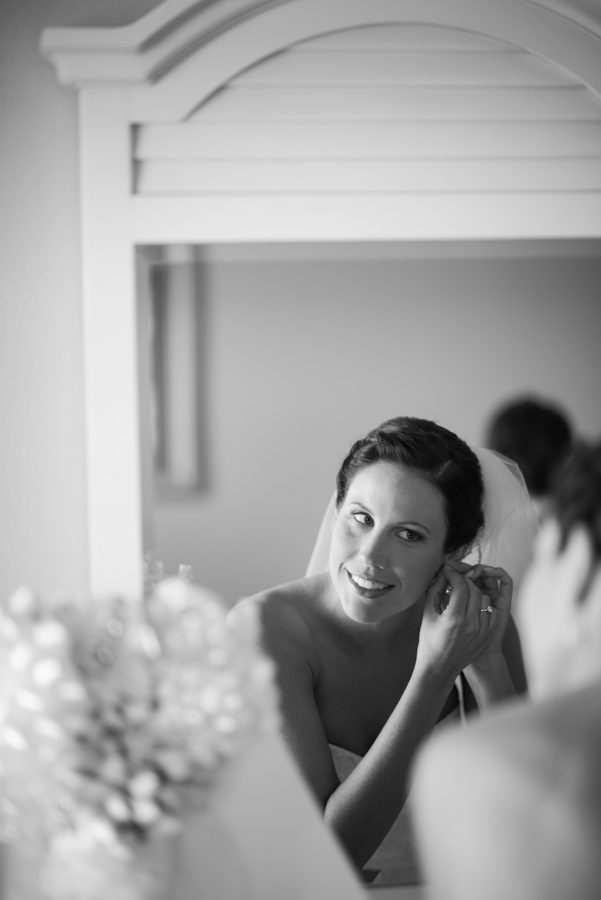 Bride puts on her earrings in the mirror before her ceremony at Herrington on the Bay in Chesapeake Beach, MD. Captured by NJ wedding photographer Ben Lau.