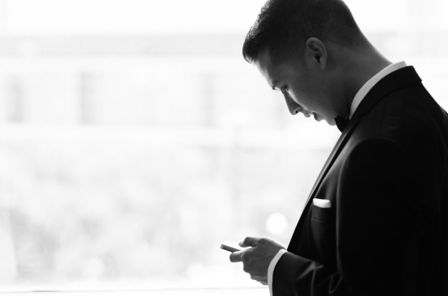 Groom looks at his phone on the morning of his wedding in Baltimore, MD. Captured by awesome Ben Lau Photography.