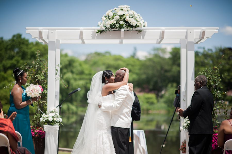 Bride and groom share a kiss near the pond at Coral House in Baldwin, NY. Captured by awesome NJ wedding photographer Ben Lau.