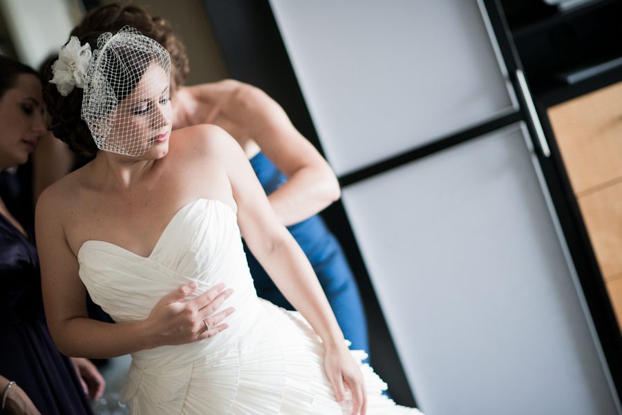 A bride is helped into her dress on her wedding day at the Heldrich Hotel in New Brunswick, NJ. Captured by awesome northern NJ wedding photographer Ben Lau.