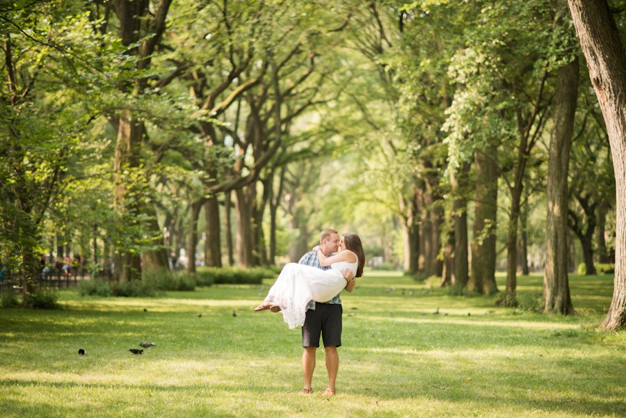 Tim poses with Kathleen in a lawned area during their engagement session in New York City's Central Park. Captured by Ben Lau Photography.