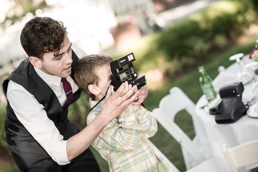 Brother in law of the bride teaches young boy how to use a camera on her wedding day on Shelter Island, NY. Captured by Northern NJ wedding photographer Ben Lau.