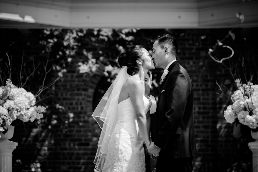 Bride and groom share their first kiss at an outdoor wedding ceremony at The Manor in West Orange, NJ. Captured by northern NJ wedding photographer Ben Lau.