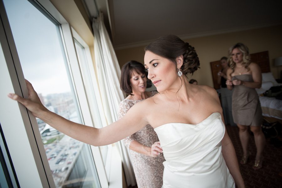 Bride Lisa looks out the window while her mother helps her into her dress on the morning of her wedding at the Baltimore Museum of Industry. Captured by Ben Lau Photography.