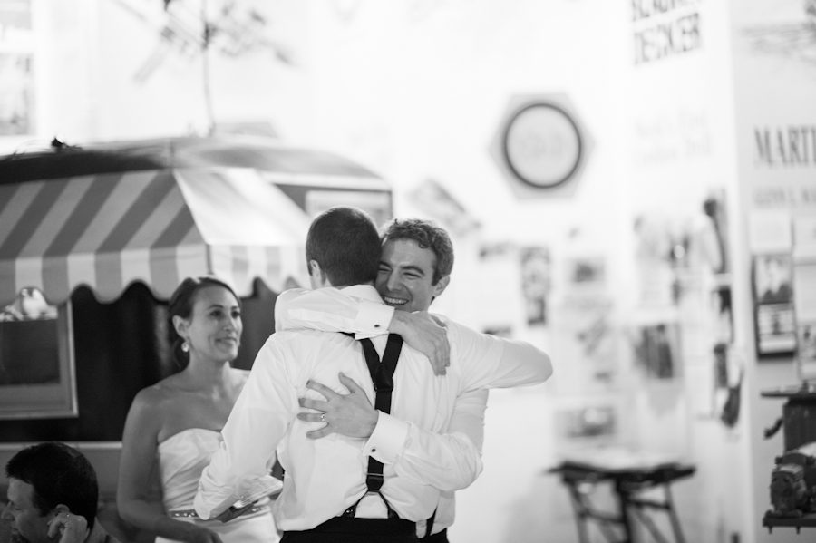 Groom and best man share a hug during Lisa and Matt's wedding reception at the Baltimore Museum of Industry in Baltimore, MD. Captured by northern NJ wedding photographer Ben Lau.