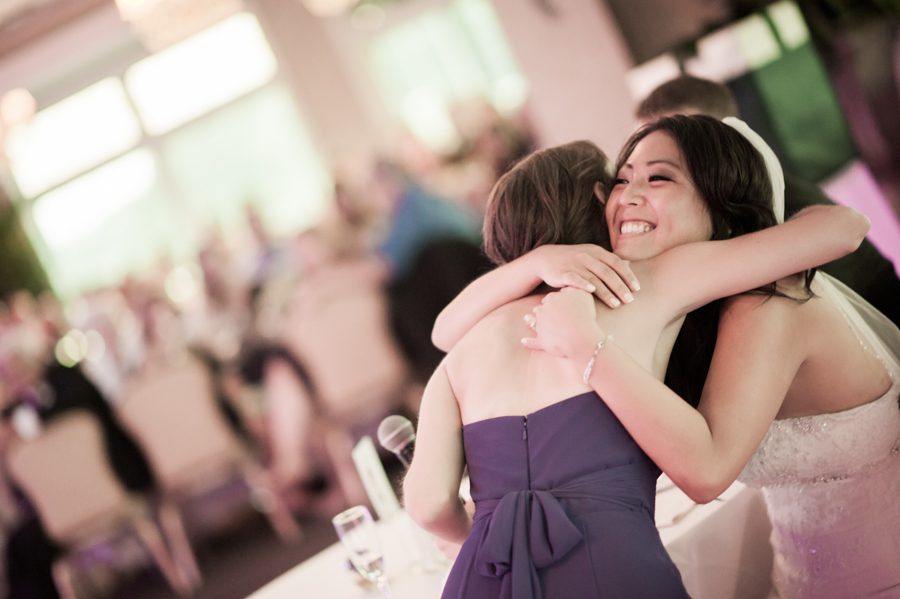 Bride hugs her sister during speeches during a wedding at the Neshanic Valley Golf Course in Neshanic Station, NJ. Captured by northern NJ wedding photographer Ben Lau.