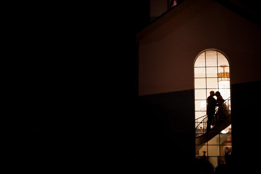 Sandra and Drew share a kiss by the window at the conclusion of their wedding reception at Perona Farms in Andover, NJ. Captured by northern NJ wedding photographer Ben Lau.