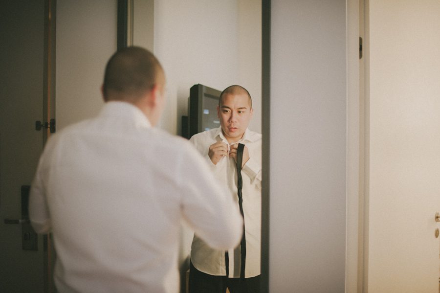 Groom adjusts his tie in his Bryant Park hotel room on his wedding day. Captured by NYC wedding photographer Ben Lau.