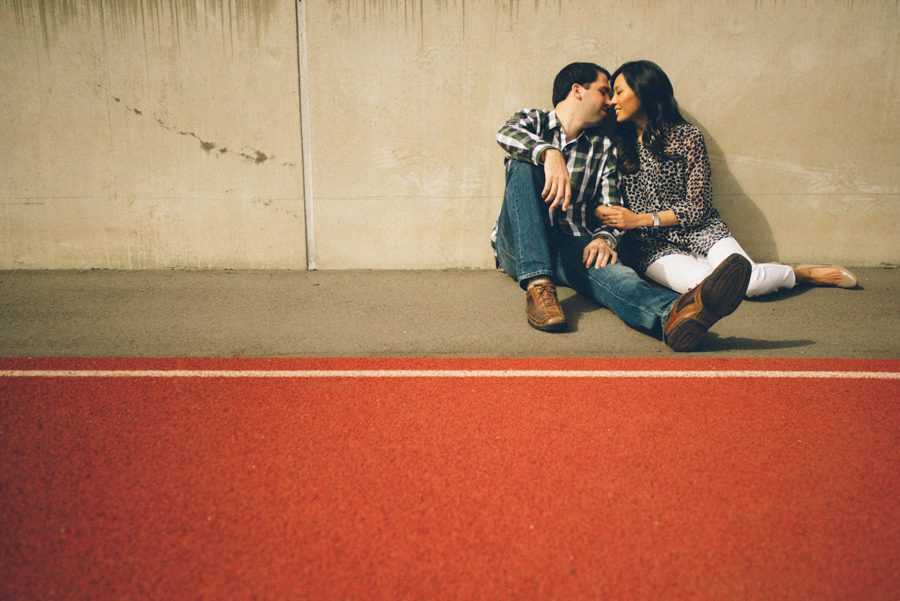 Julia and Jeff pose against a wall on a track during their engagement session at a Princeton University.