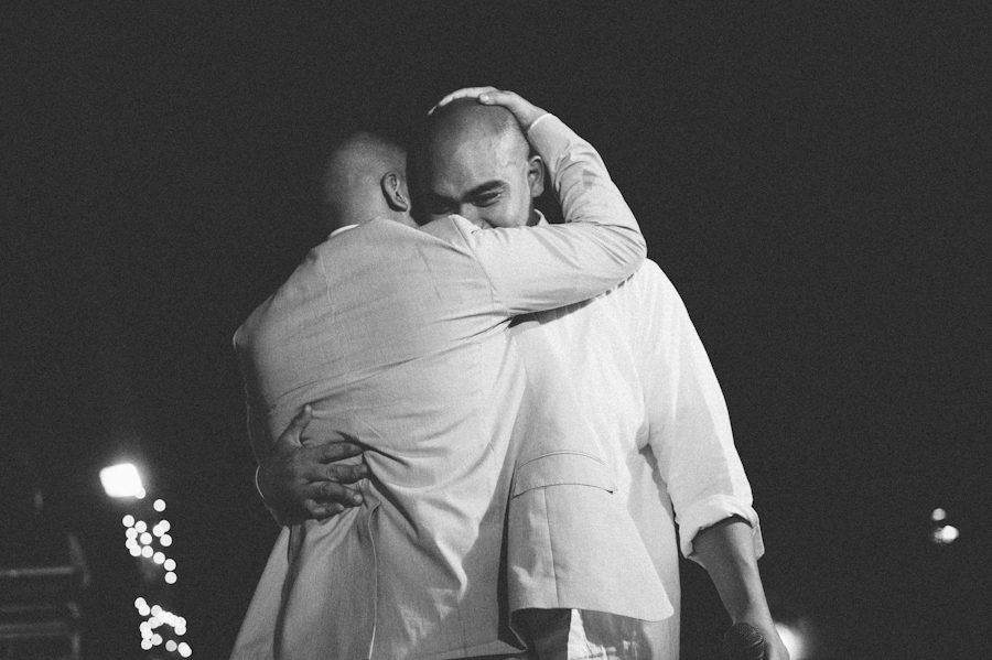 Groom and best man hug during speeches at a Radisson Aruba wedding reception. Captured by destination wedding photographer Ben Lau.