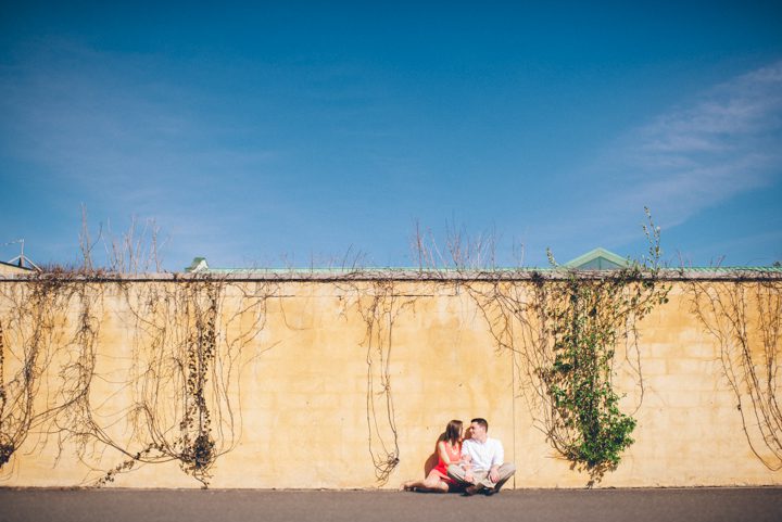 Couple sits against a wall during their engagement session at the Grounds for Sculpture in Hamilton, NJ. Captured by NJ wedding photographer Ben Lau.