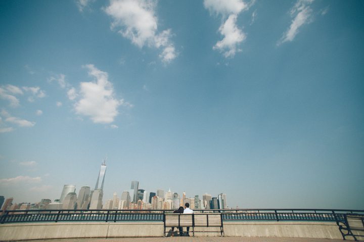 Couple sits on a bench and views the NYC skyline during their engagement session in Jersey City with NYC wedding photographer Ben Lau.