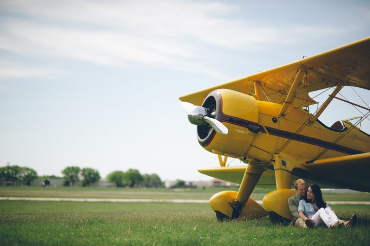 Couple sits against a biplane during their engagement session at an airfield in Philadelphia, PA. Captured by NJ wedding photographer Ben Lau.