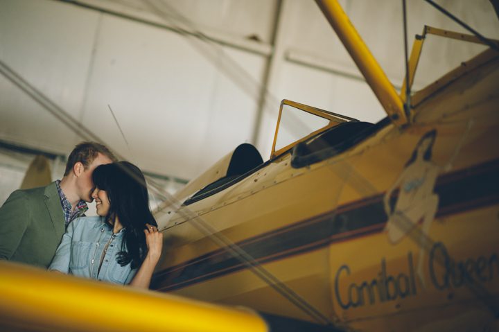 Couple poses against a biplane during their engagement session at an airfield in Philadelphia, PA. Captured by NJ wedding photographer Ben Lau.