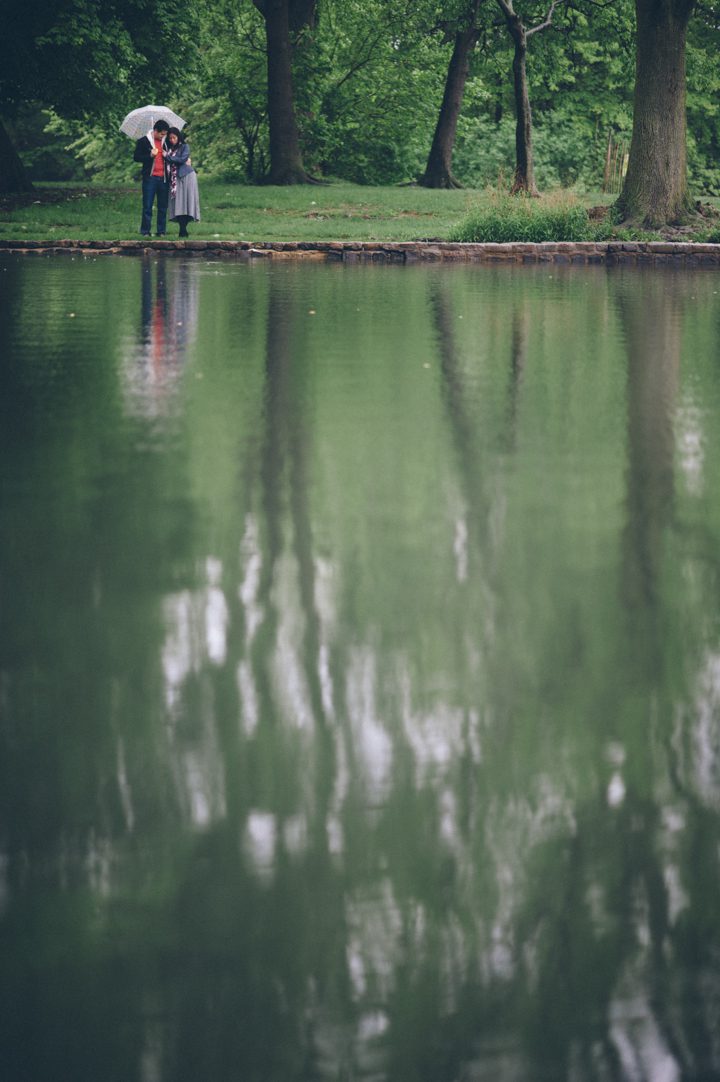 A couple stand by a lake with an umbrella during their rainy engagement session in Prospect Park with NYC wedding photographer Ben Lau.