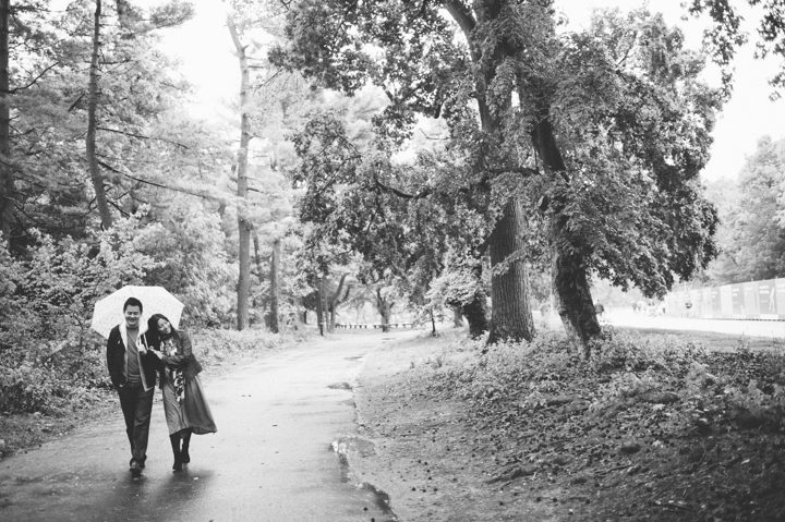 Couple walk along a path with an umbrella during their rainy engagement session in Prospect Park with NYC wedding photographer Ben Lau.