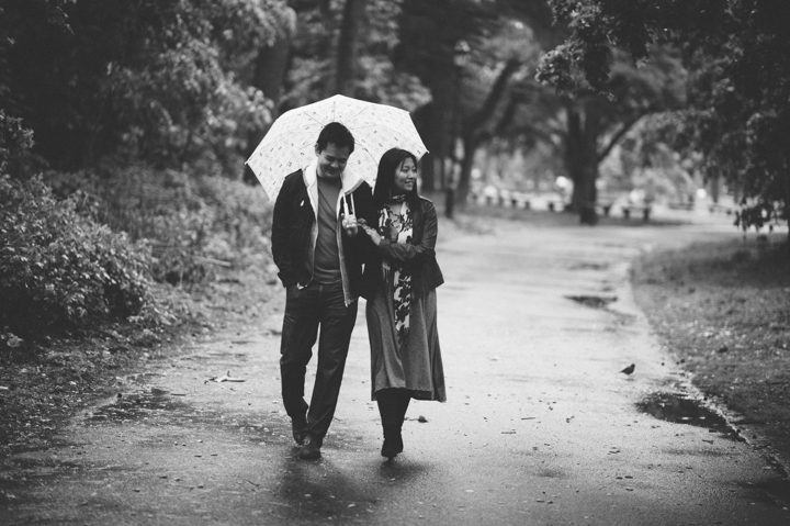A couple walks along a path with an umbrella during their rainy engagement session in Prospect Park with NYC wedding photographer Ben Lau.