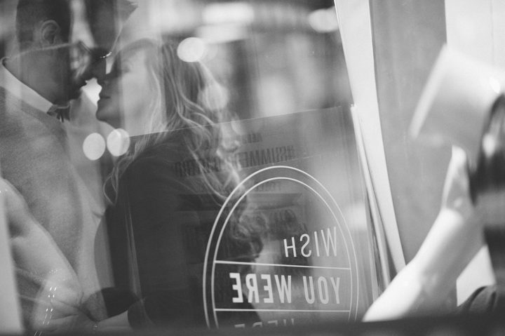 A couple kisses through a window in Times Square during their engagement session with NYC wedding photographer Ben Lau.