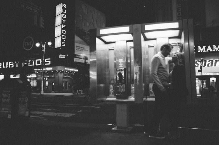 A couple kisses inside a telephone booth in Times Square during their engagement session with NYC wedding photographer Ben Lau.