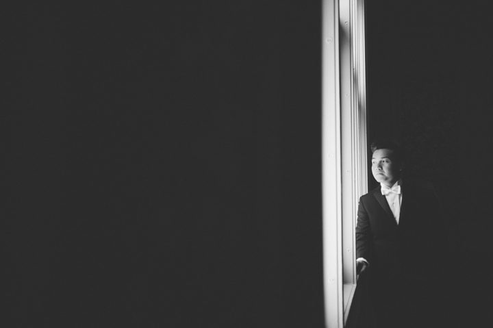 Groom looks out of the window on the morning of his wedding at the Hempstead House in Sands Point Preserve, Long Island. Captured by NYC wedding photographer Ben Lau.