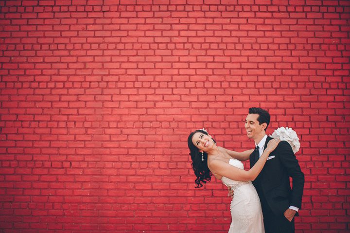 Couple poses by a painted red brick wall in Red Hook, Brooklyn. Captured by NYC wedding photographer Ben Lau.