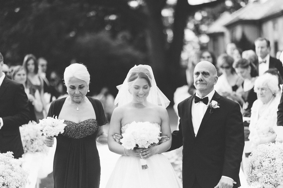 Bride walks down the aisle with her parents during a wedding at the Castle on the Hudson in Tarrytown, NY. Captured by NYC wedding photographer Ben Lau.