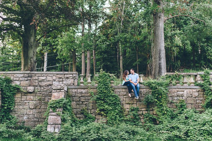 Couple sits on a stone wall during their engagement session in Morristown with NJ wedding photographer Ben Lau.