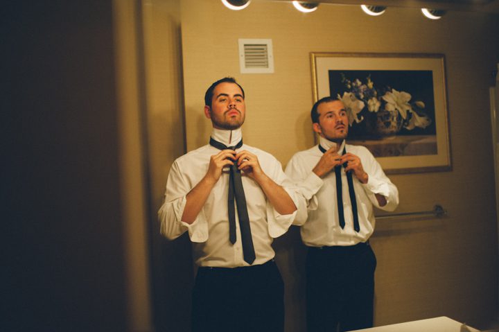Groomsmen tie their ties in the mirror on the morning of a wedding at the Stone House in Stirling Ridge. Captured by NJ wedding photographer Ben Lau.