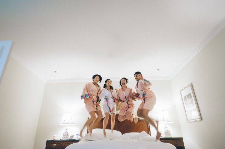 Brides and bridesmaids jump on the bed at the Ritz Carlton in San Francisco, CA. Captured by NYC wedding photographer Ben Lau.