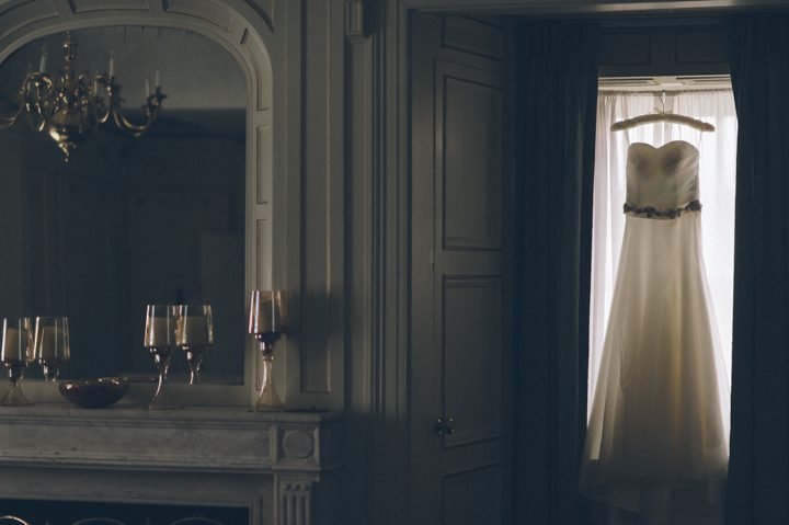Wedding dress hangs in a window at Tappan Hill Mansion in Tarrytown, NY. Captured by NYC wedding photographer Ben Lau.