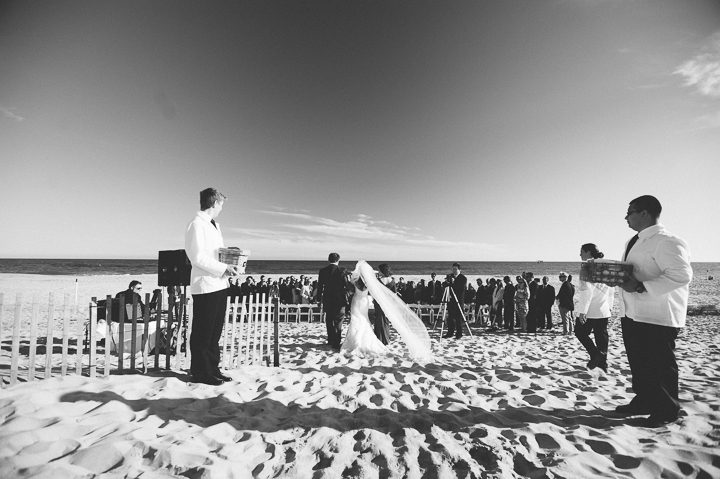 Bride walks down the aisle with her parents during her beach wedding ceremony at Westhampton Bath & Tennis in Westhampton, NY. Captured by NYC wedding photographer Ben Lau.