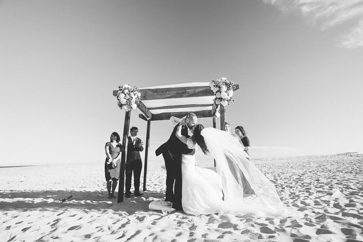 Groom kisses bride during a beach wedding ceremony at Westhampton Bath & Tennis in Westhampton, NY. Captured by NYC wedding photographer Ben Lau.