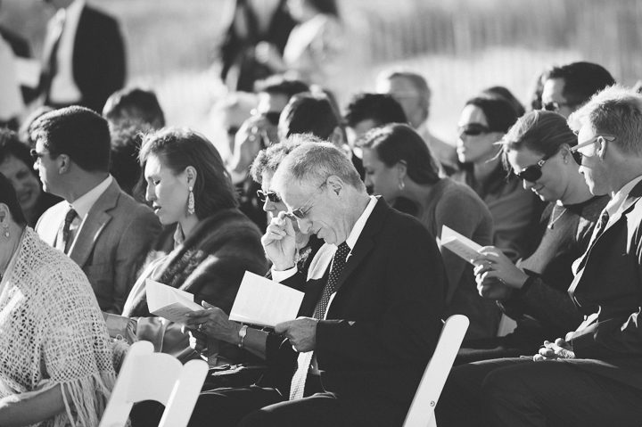 Guests read their programs during a wedding ceremony at Oceanblue/Westhampton Bath & Tennis in Westhampton, NY. Captured by NYC wedding photographer Ben Lau.