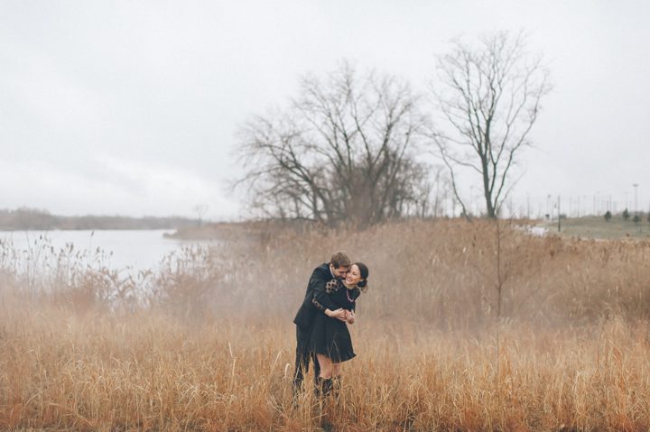 Zoie and Daniel embrace each other in a field during their rainy day engagement session with New York City wedding photographer Ben Lau.