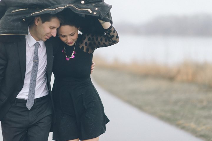 Couple shields themselves from the rain at Overpeck Park during their rainy day engagement session with New York City wedding photographer Ben Lau.