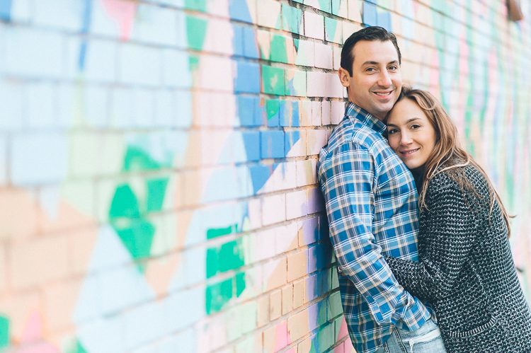 Couple poses along a wall, during their engagement session in Williamsburg, with NYC wedding photographer Ben Lau.