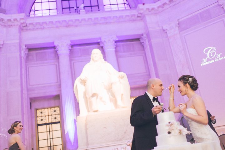 Bride and groom cut the cake during their wedding reception at the Franklin Institute in Philadelphia. Captured by NYC wedding photographer Ben Lau.