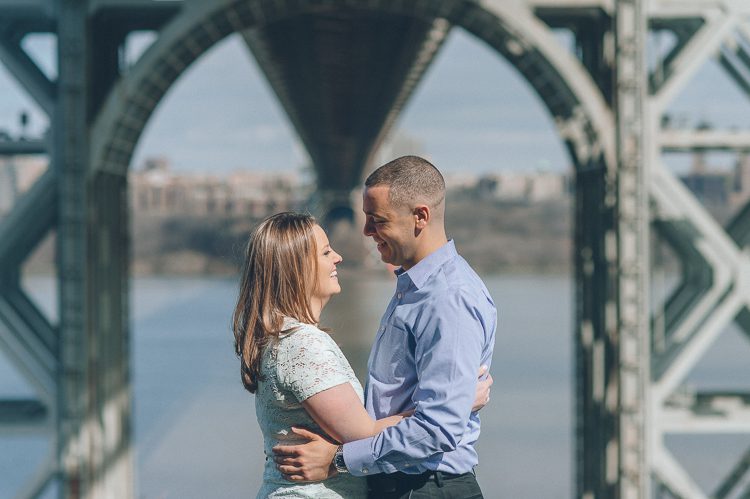 A couple poses under the GW bridge during their engagement session in Palisades Park, NJ. Captured by NJ wedding photographer Ben Lau.