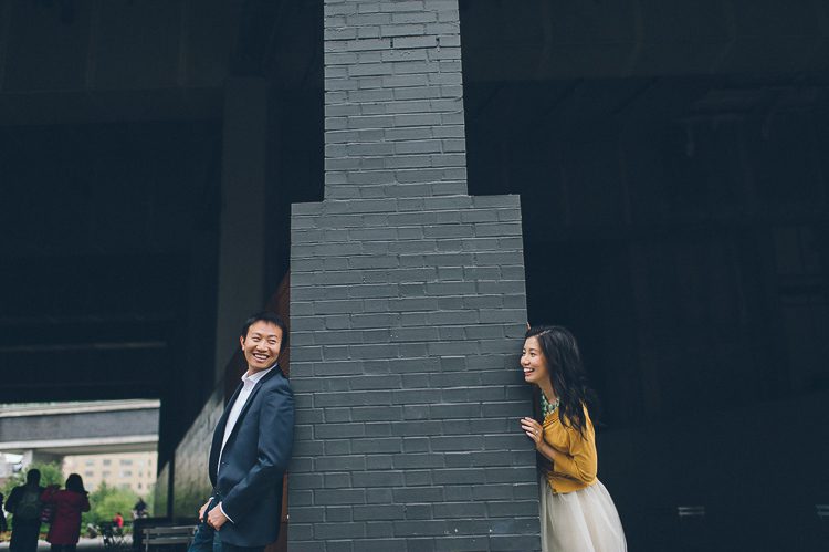 Alyssa peeks around the corner during their engagement session at the High Line in NYC. Captured by NYC wedding photographer Ben Lau.